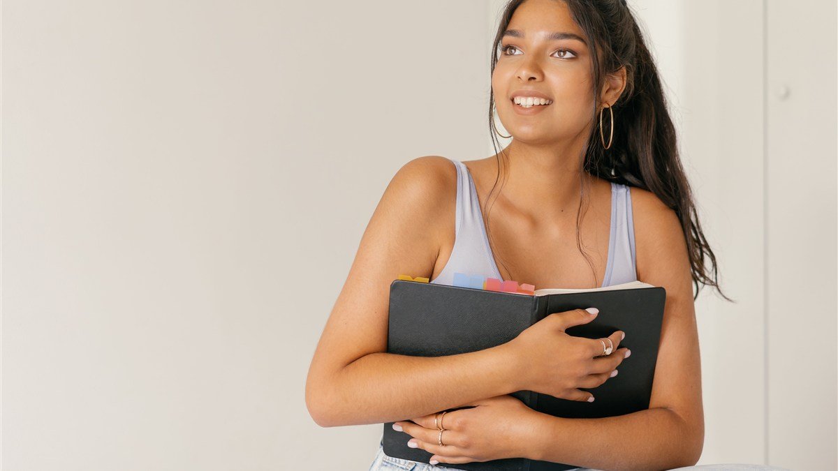 Mulher sorrindo segurando um planner com abas coloridas, pensando em como organizar as finanças sem salário fixo
