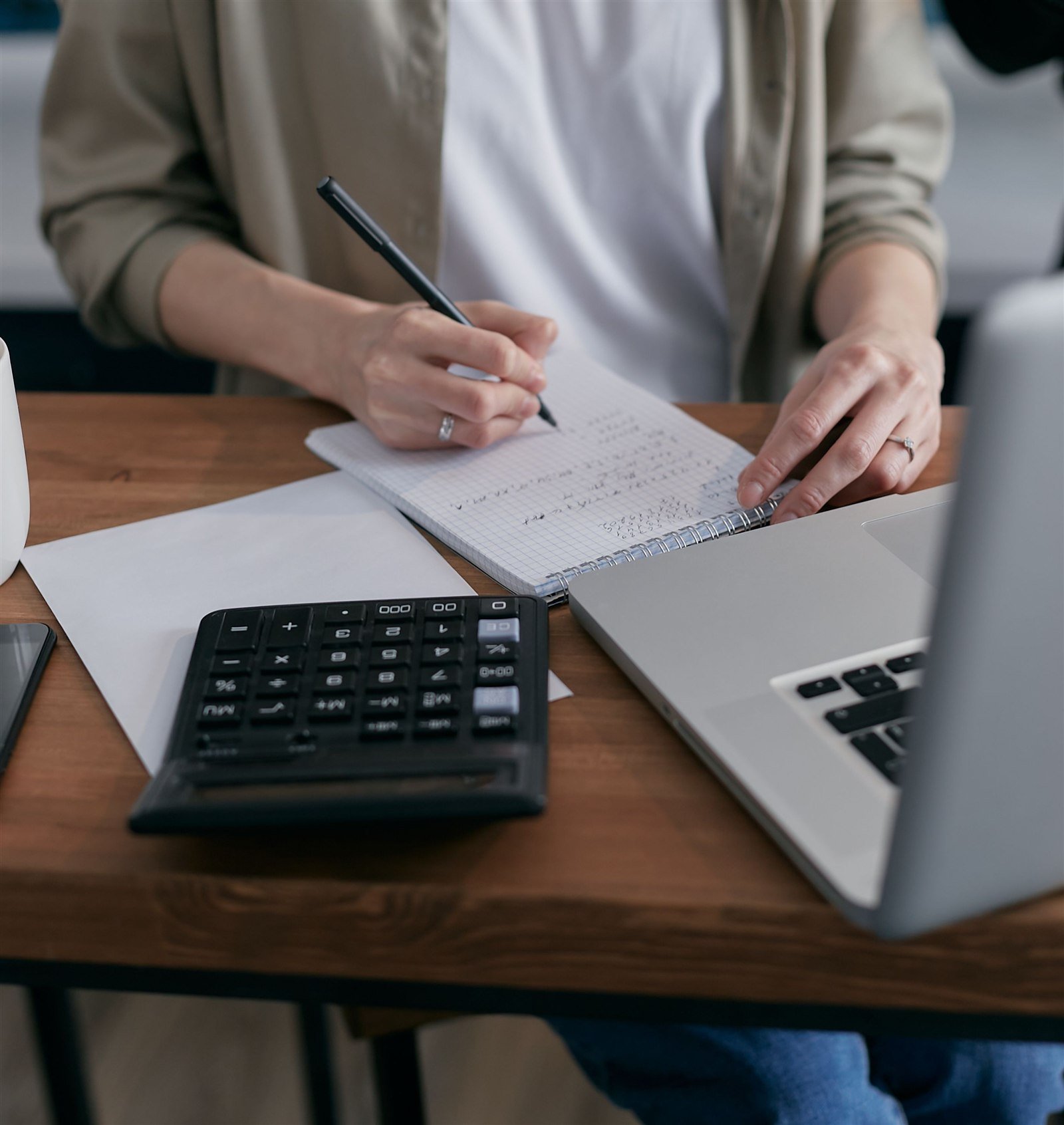 Mulher fazendo contas com calculadora e caderno de anotações na mesa