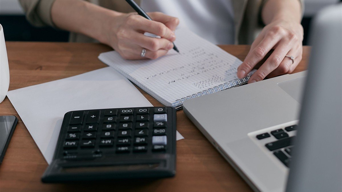Mulher calculando as fatias do orçamento no caderno com calculadora ao lado