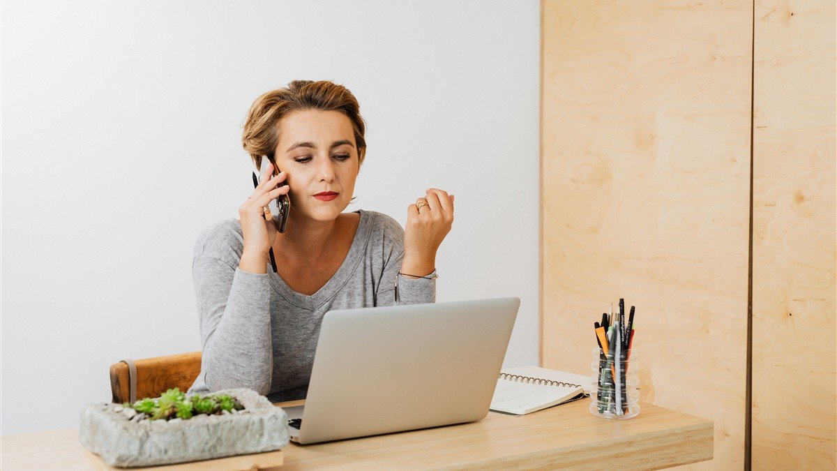 Mulher decidindo entre planilha no notebook e aplicativo no celular para controlar as finanças