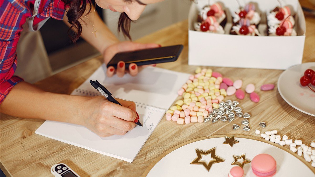 Confeiteira autônoma anotando o custo dos ingredientes de uma receita no caderno
